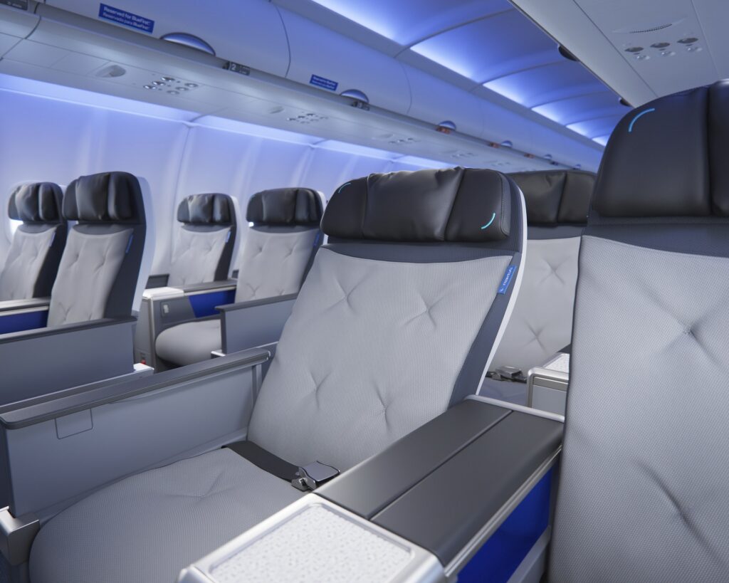 Rows of wide BlueFirst seats, including a seat shown in a reclined position, beneath blue cabin lighting.
