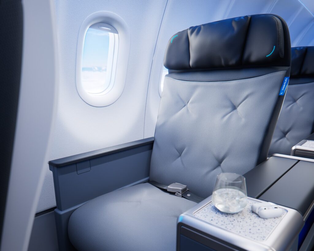A BlueFirst window seat with gray upholstery, a black cushioned headrest, wide armrests, and a Tuft & Needle tag.