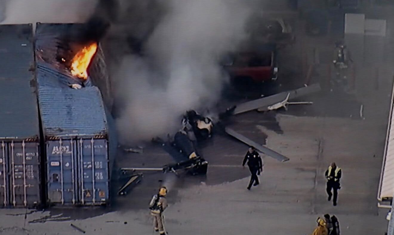 Photo showing the crashed helicopter in flames after crashing into containers.