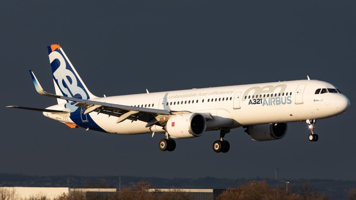 Airbus A321neo in manufacturer house colours approaching to land against a dark sky.