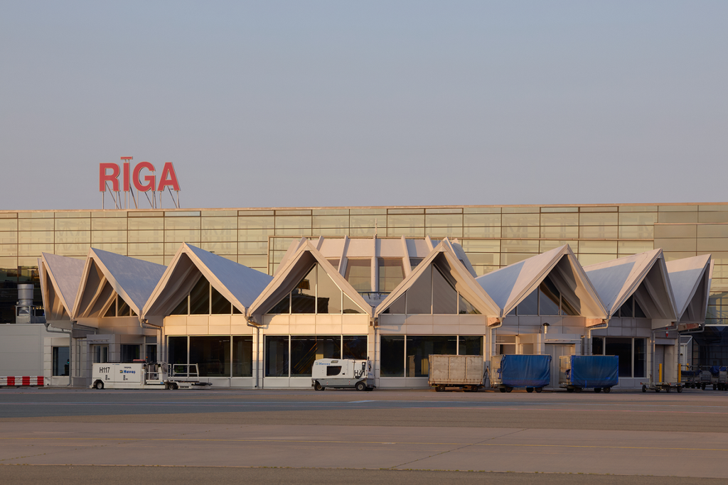 Airside view of Riga Airport’s terminal building, with ground-service vehicles parked beside its distinctive angular roof.