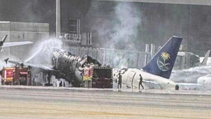 Firefighters spray water onto a severely burnt Saudia aircraft beside an airport terminal, with smoke rising from its exposed fuselage.